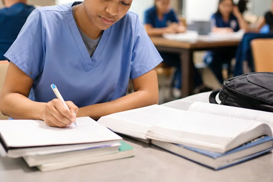 A nursing student in scrubs with a textbook